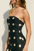 Woman wearing a black strapless maxi dress with large beige polka dots and delicate gold jewelry