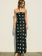 Woman wearing a strapless black maxi dress with large white polkadots standing against a light wall