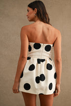 Woman wearing a strapless mini dress with large black polkadots on cream fabric, viewed from the back