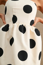 Close-up of a fitted women's dress with large black polkadots on cream fabric, featuring a gathered waist detail.