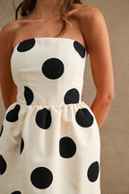 Close-up of a strapless women's dress with large black polkadots on cream fabric.