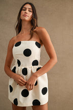 Woman wearing strapless white mini dress with large black polkadots in a neutral setting