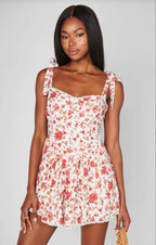Woman wearing a white floral romper with adjustable tie straps and smocked back in women's clothing fashion.