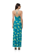 Woman wearing a teal maxi dress with green cherry print and thin crossed straps, styled for women's clothing.