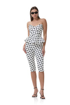Woman wearing white cropped pants with black polka dots paired with a matching strapless peplum top and sunglasses