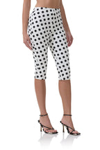 Woman wearing white capri pants with black polka dots paired with black high-heeled sandals in women's clothing style.