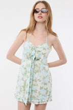 Woman wearing sleeveless floral halter mini dress with tie neck and bow detail in pastel colors