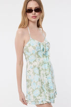 Woman wearing sleeveless floral halter mini dress with tie neck and sunglasses in a studio setting