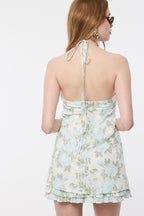 Woman wearing sleeveless halter mini dress with blue floral print and tie neck, shown from the back