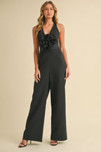 Woman wearing a black wide-legged jumpsuit with a plunging neckline and large floral detail at the waist.