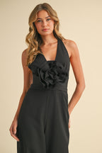 Woman wearing a black wide-legged jumpsuit with a plunging neckline and large fabric rosette detail on front