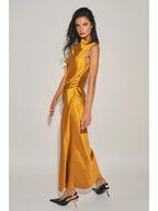 Woman wearing a golden satin maxi dress with an asymmetrical neckline and cap sleeve standing against a plain background.