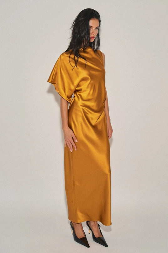 Woman wearing a mustard satin maxi dress with an asymmetrical neckline and one cap sleeve in a studio setting