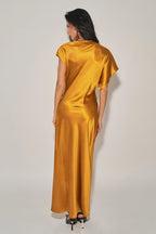 Woman wearing a golden satin asymmetrical maxi dress with cap sleeve and flowy silhouette from the back