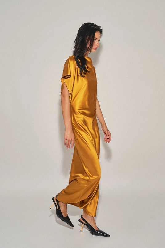 Woman wearing a golden satin asymmetrical maxi dress with one sleeve paired with black pointed heels.