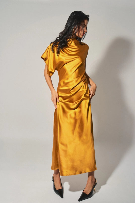 Woman wearing a golden satin asymmetrical maxi dress with draped neckline and single sleeve in women's clothing.
