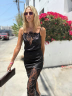 Woman wearing a black satin and lace camisole top walking outdoors in sunny weather with sunglasses and clutch bag