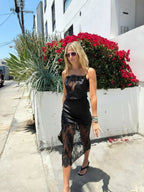 Woman wearing a black satin and lace dress walking outdoors near a bright red flower bush in women's clothing style
