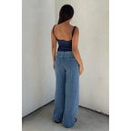 Woman wearing a navy scoop neck tank top paired with wide-leg blue denim jeans against a plain wall background.