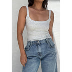Woman wearing a light gray scoop neck tank top paired with high-waisted blue jeans in casual women's clothing style