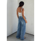 Woman wearing a white scoop neck tank top paired with loose-fitting blue jeans in a simple room.