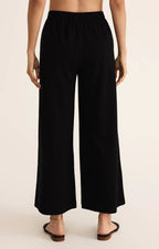 Back view of a woman wearing relaxed fit black wide-leg flare pants with elastic waistband in cotton jersey fabric.