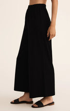 Woman wearing black wide flare pants with elastic waistband and black slide sandals against neutral background
