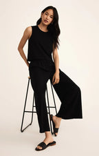 Woman wearing black wide flare pants with elastic waistband and sleeveless black top sitting on stool