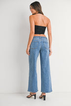 Woman wearing high-waisted, wide leg denim jeans and black strapless top, shown from back in a studio.