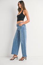 Woman wearing high-waist wide leg denim jeans with seams, black sleeveless crop top, and black heeled sandals against white background.