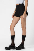 Woman wearing black tailored shorts with button and zip closure styled with sheer black socks and black shoes
