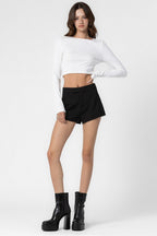 Woman wearing black lined shorts with button closure and white long-sleeve crop top paired with black platform boots