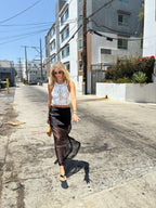 Woman wearing a black sheer overlay midi skirt and white crochet sleeveless top walking on sunny urban street