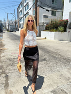 Woman wearing a black sheer overlay midi skirt paired with a white crochet crop top walking outdoors