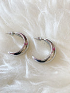 Pair of chunky silver dipped crescent hoop earrings on soft white fabric background