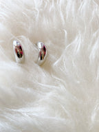 Chunky silver huggie hoop earrings displayed on a soft white textured fabric background.