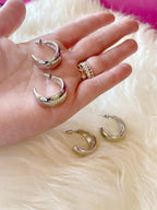 Chunky silver hoop earrings shown on a hand and soft white surface, styled with delicate rings for women's fashion.