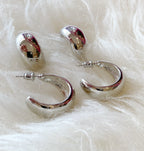 Chunky silver hoop and small huggie earrings displayed on soft white fabric, stylish women's accessory.