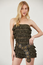 Woman wearing a strapless ruffled romper with glittery fabric and a decorative wide belt in women’s clothing style.