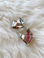 Pair of shiny silver sculpted post-back earrings on soft white textured fabric background