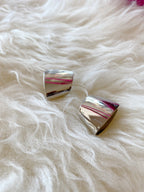 Pair of shiny silver sculpted earrings with post backs displayed on soft white fur background