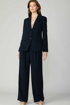 Woman wearing a fitted single-breasted black blazer with welt pockets and matching wide-leg trousers in women's clothing.
