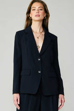 Woman wearing a fitted black single-breasted blazer with welt pockets, styled with layered gold necklaces