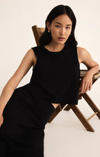 Woman wearing a black sleeveless crew neck muscle tank in a relaxed fit, leaning on a wooden chair