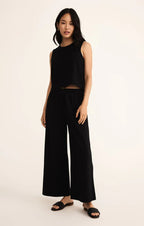 Woman wearing a black sleeveless crew neck muscle tank with wide-leg black pants in a casual outfit.
