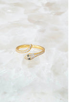 Delicate gold vermeil snake ring with sparkling stones on a textured light background for women's fashion accessory.