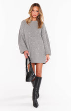 Woman wearing a gray long-sleeve sweater dress with sequin detail paired with black knee-high boots and a black handbag