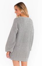 Woman wearing a grey knit sweater dress with long sleeves and small bead accents, shown from the back.
