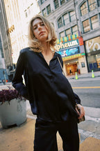 Woman wearing a dark pinstripe blouse and pants standing on a city sidewalk near a theater marquee.
