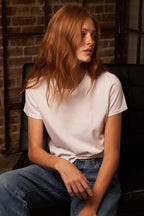 Woman with red hair wearing a white mid-weight cotton tee and blue jeans sitting on a black chair indoors